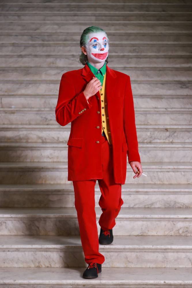 L'attore truccato da Joker scende una scalinata di marmo, con una mano al bavero della giacca rossa