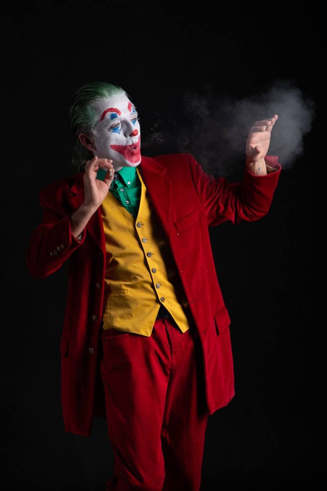 Joker di profilo che soffia il fumo verso la mano aperta, su fondo nero